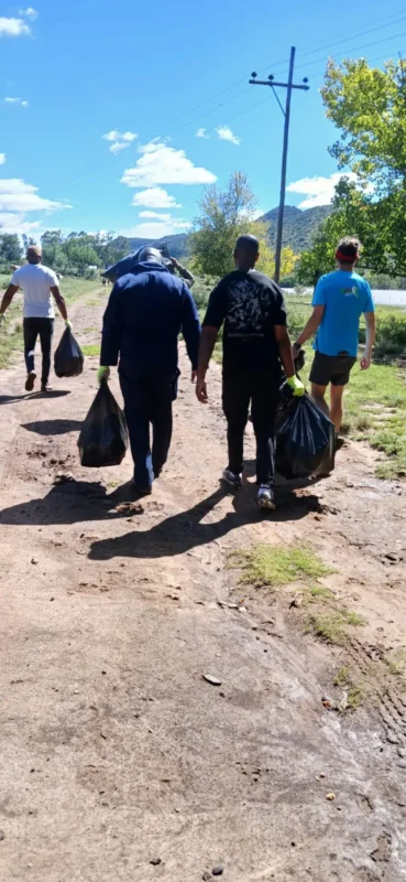 Four volunteers walk along the gravel road at JL de Bruin Dam carrying full black refuse bags.